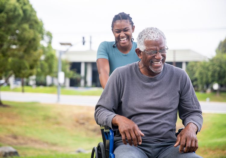 older man in wheelchair with a younger woman pushing him outdoors