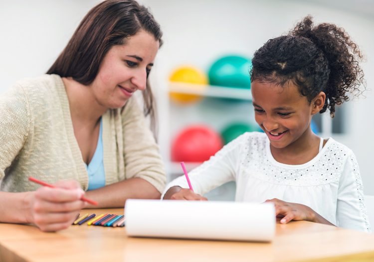 young girl coloring with an woman looking at her work