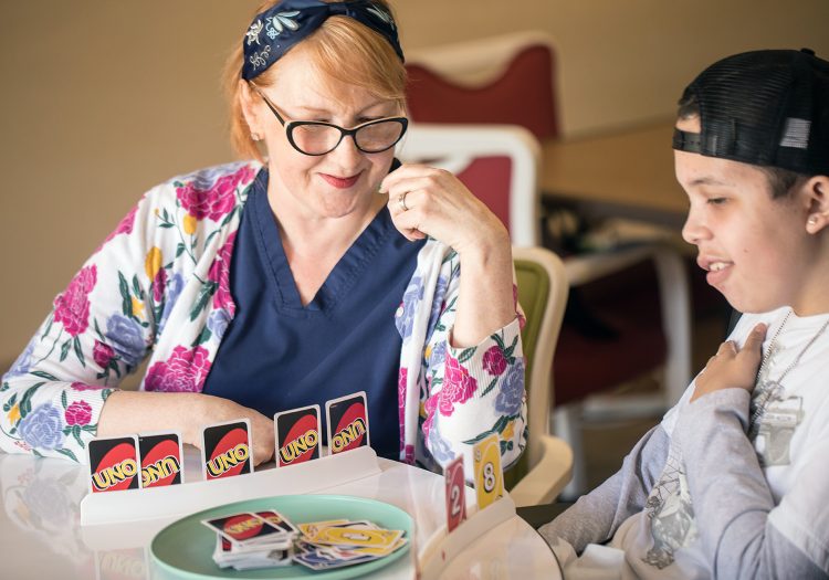 older woman with adolescent boy in wheelchair playing Uno at a table