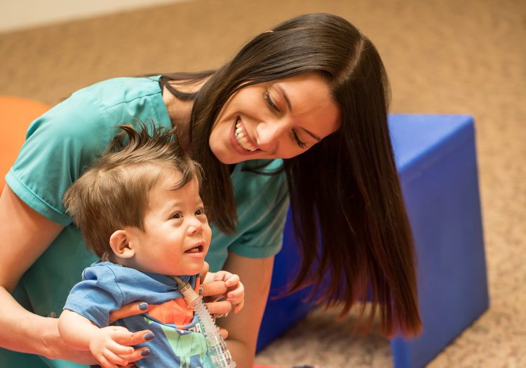 young boy being held by a female physical therapist smiling down on him
