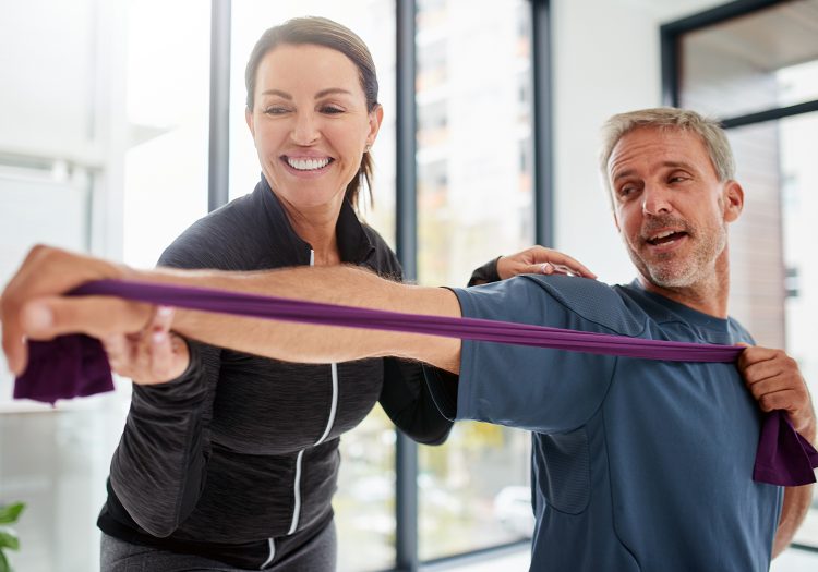 man holding a resistance band while a female physical therapist guides him